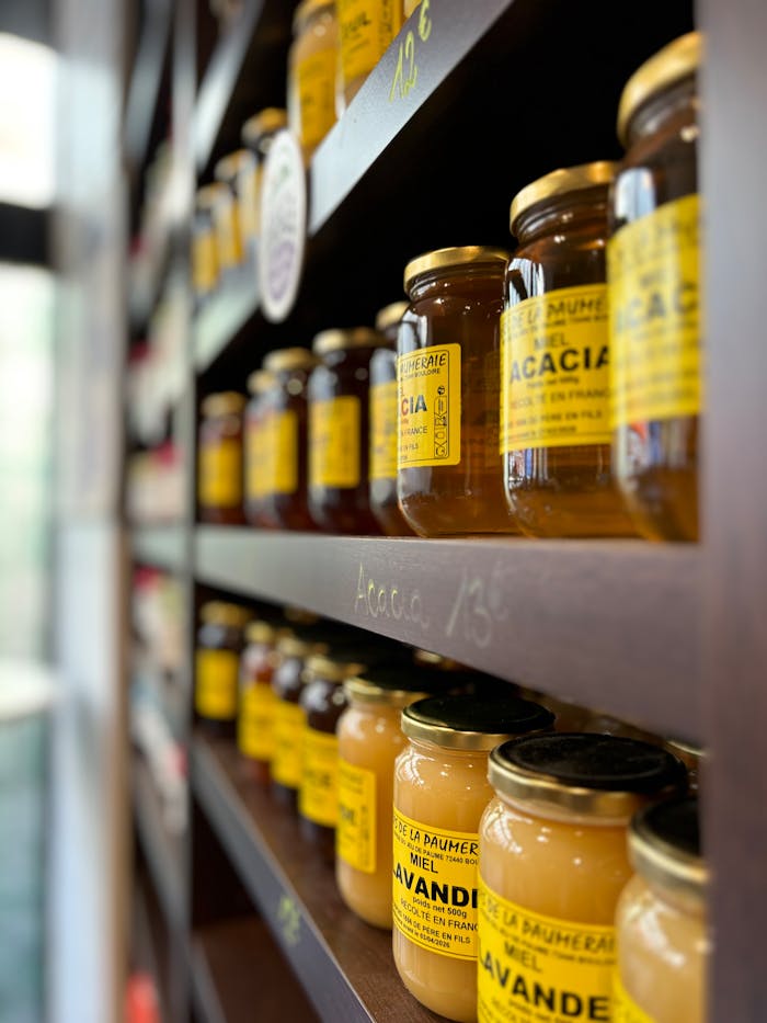 Rows of honey jars with yellow labels neatly stacked on wooden shelves in a Paris shop.