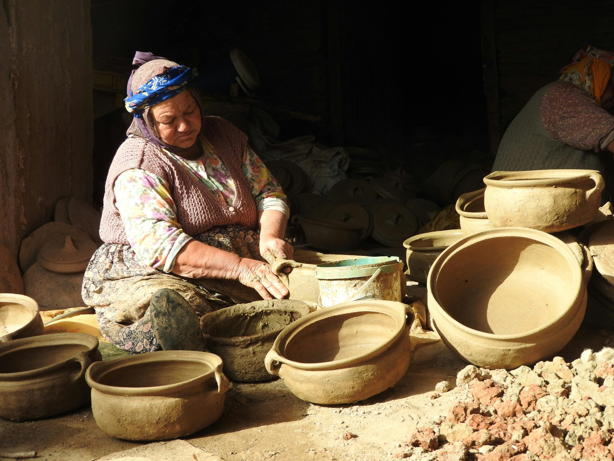 An elderly woman skillfully shaping clay pots in a rustic workshop. Natural lighting adds to the artisan atmosphere.